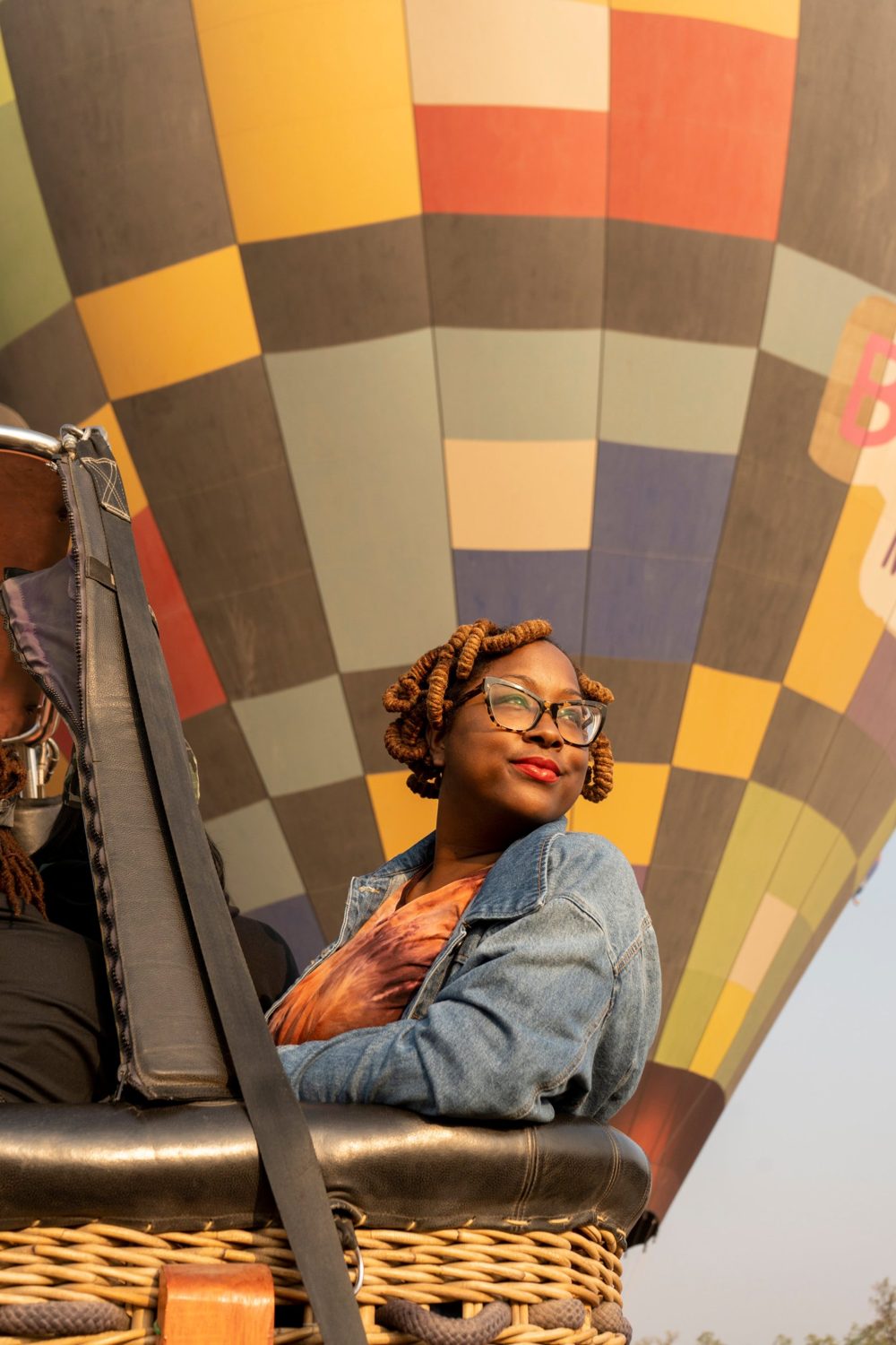 Valicia smiling in a hot air balloon basket in front of a colorful checkered balloon