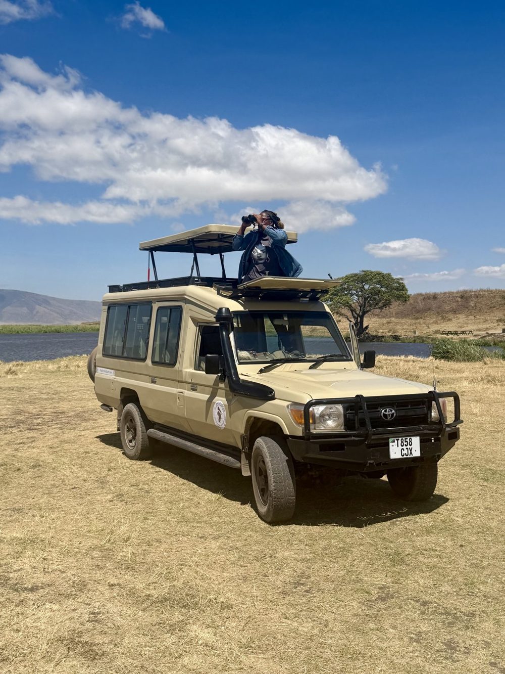 Valicia looking through binoculars from the pop-top roof of a safari Land Cruiser